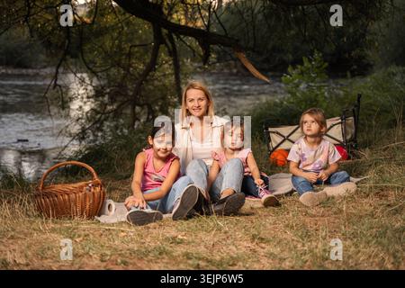 Mère et filles profitant d'un pique-nique au bord de la rivière Banque D'Images
