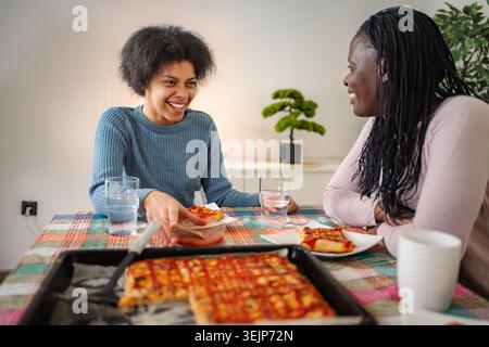Jeunes femmes noires mangeant de la pizza, partageant un moment heureux Banque D'Images