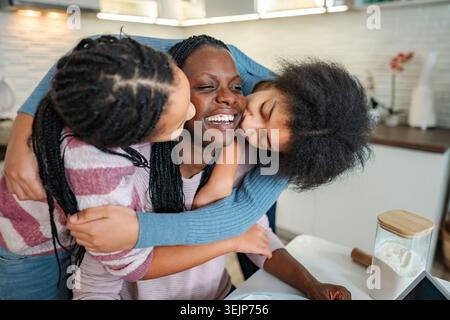 Heureuse mère noire riant pendant que les filles l'embrassent et l'embrassent Banque D'Images