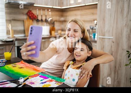 Mère et fille appréciant le temps d'art ensemble tout en prenant un selfie dans leur cuisine lumineuse Banque D'Images