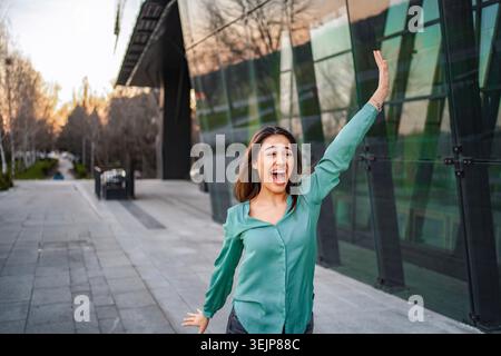 Femme d'affaires excitée célébrant le succès devant l'immeuble de bureaux moderne Banque D'Images