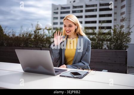 Femme d'affaires ayant l'appel vidéo sur ordinateur portable à l'extérieur ondulant Banque D'Images