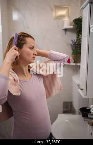Femme enceinte peignant ses cheveux dans la salle de bain après la douche Banque D'Images