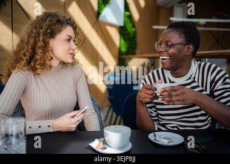 Deux jeunes femmes adultes riant et parlant dans un café Banque D'Images