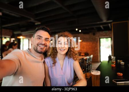 Jeune couple joyeux prenant selfie au comptoir du bar Banque D'Images
