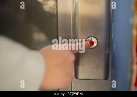 Main appuyant sur un bouton d'ascenseur dans un couloir de bâtiment moderne Banque D'Images