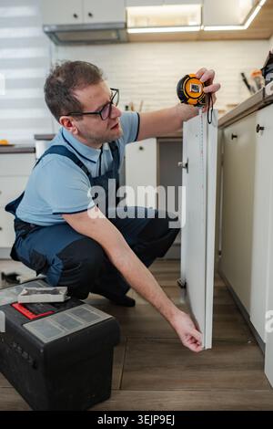 Bricoleur mesurant la porte de l'armoire de cuisine pour la réparation Banque D'Images