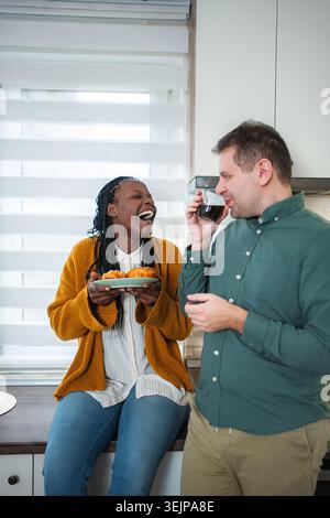 Heureux couple multiracial appréciant le café et les pâtisseries dans la cuisine Banque D'Images