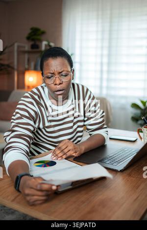 Femme noire se concentrant sur le rapport financier important au bureau à domicile Banque D'Images