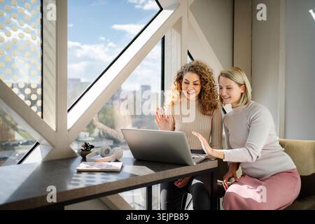 Deux femmes appelant vidéo sur ordinateur portable agitant les mains Banque D'Images
