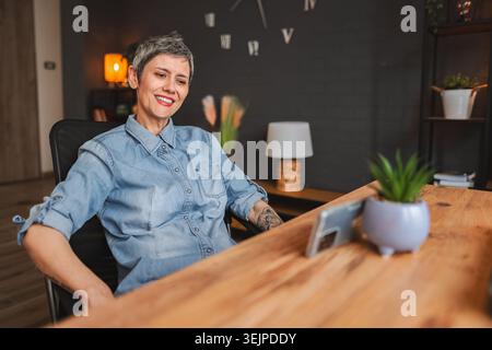 Femme d'affaires mature souriante ayant un appel vidéo dans le bureau à domicile Banque D'Images