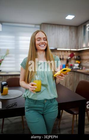 Femme heureuse profitant d'une boisson rafraîchissante dans une cuisine confortable Banque D'Images