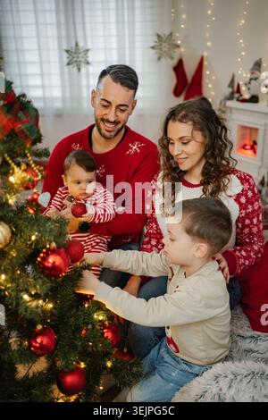 Famille décorant l'arbre de Noël ensemble célébrant les vacances d'hiver à la maison Banque D'Images