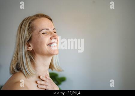 Femme blonde heureuse riant avec les yeux fermés et la main sur la poitrine Banque D'Images