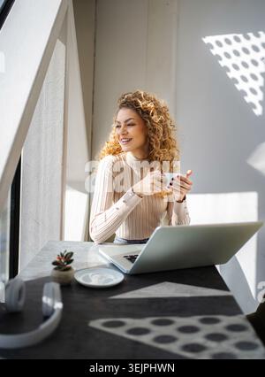 Heureuse jeune femme buvant du café s'arrêtant au travail Banque D'Images