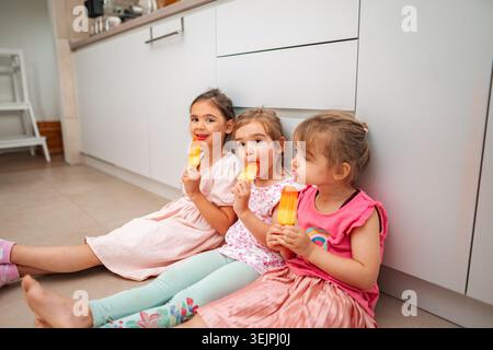 Trois filles appréciant les popsicles dans une cuisine confortable Banque D'Images