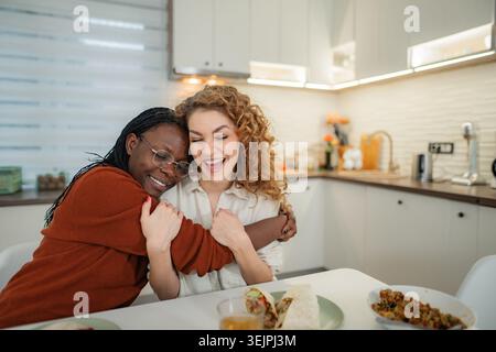 Amies embrassant rire ensemble dans la cuisine Banque D'Images