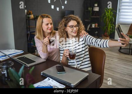Deux collègues femmes prennent des selfies et boivent du café Banque D'Images