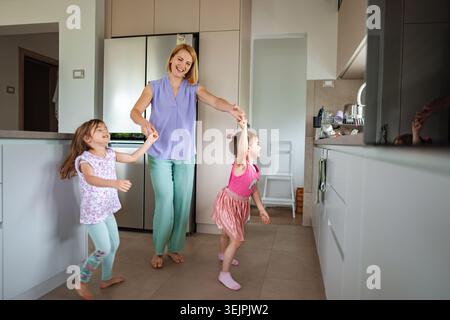 Une femme tourne joyeusement deux enfants dans une cuisine lumineuse. Banque D'Images