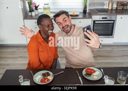 Couple heureux prenant Selfie tout en prenant le petit déjeuner dans la cuisine Banque D'Images