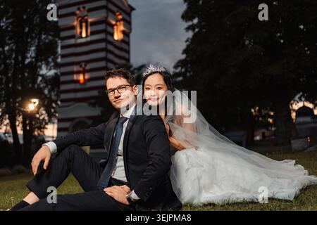 Couple de mariage interracial assis sur l'herbe au crépuscule Banque D'Images