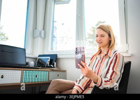 Femme faisant un appel vidéo sur smartphone travaillant à domicile Banque D'Images