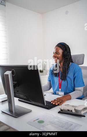 Travailleuse de santé souriante tout en travaillant sur un ordinateur avec un casque Banque D'Images