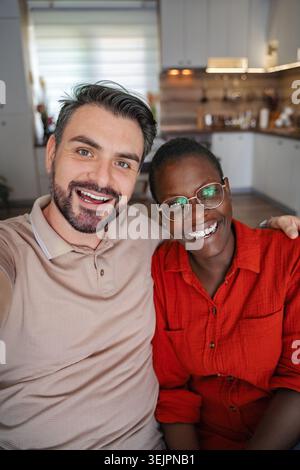 Jeune couple multi-ethnique prenant un selfie assis sur le canapé à la maison Banque D'Images