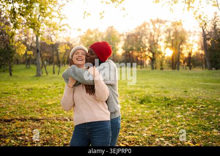 Couple diversifié partageant un baiser d'amour dans le parc d'automne Banque D'Images