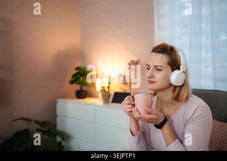Femme relaxant écoutant de la musique avec des écouteurs et du café Banque D'Images