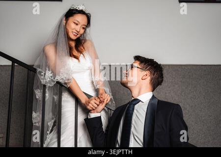 Couple interracial célébrant mariage tenant la main sur les escaliers Banque D'Images