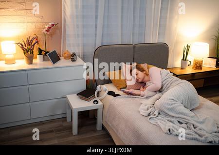 Femme s'endormant dans le lit doomscrolling téléphone la nuit Banque D'Images