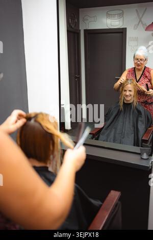 Coiffeur coiffant les cheveux de la femme dans le miroir de salon réflexion Banque D'Images
