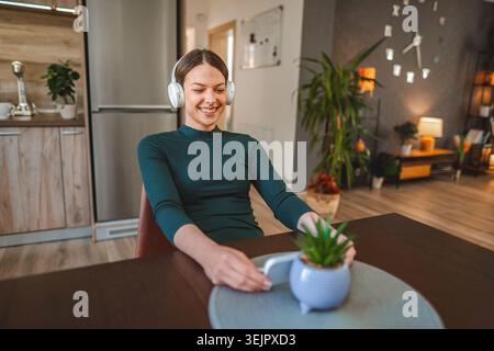 Jeune femme appréciant la musique sur les écouteurs sans fil à la maison Banque D'Images