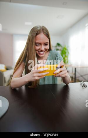 Moment joyeux d'une jeune femme s'engageant avec un téléphone dans un espace lumineux Banque D'Images