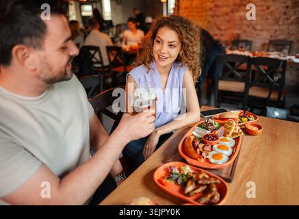 Couple toast avec des verres à bière tout en déjeunant dans un restaurant Banque D'Images