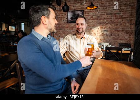 Amis qui grillent des verres à bière en profitant de la soirée pub Banque D'Images