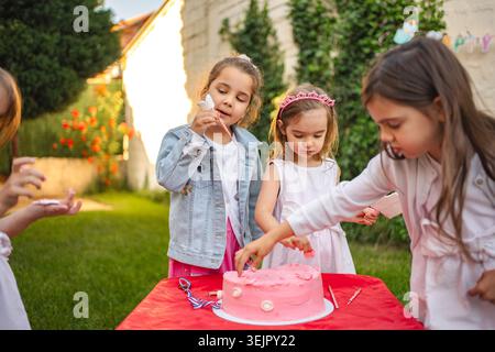 Les enfants célèbrent avec un gâteau joyeux décorant un jour ensoleillé Banque D'Images