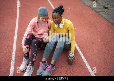 Amies féminines se relaxant sur la piste en regardant le téléphone Banque D'Images