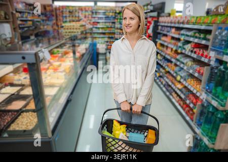 Jeune femme magasinant pour l'épicerie dans l'allée de supermarché Banque D'Images