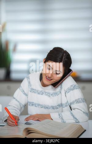 Femme multitâche étudiant, parlant au téléphone avec surligneur et écrivant Banque D'Images