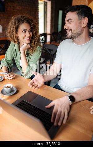 Jeune couple heureux parlant et travaillant sur ordinateur portable dans le café Banque D'Images