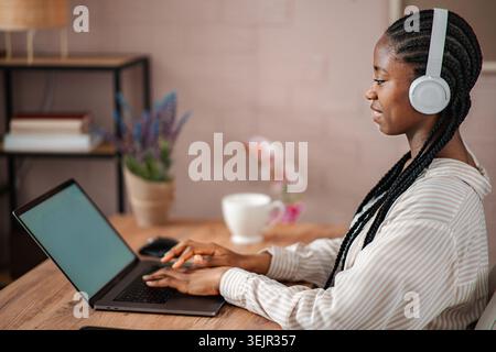 Femme noire portant des écouteurs travaillant sur ordinateur portable Banque D'Images