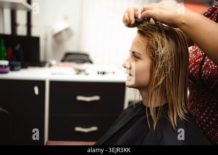 Coiffeur peignant les cheveux blonds mouillés du client au salon de beauté Banque D'Images