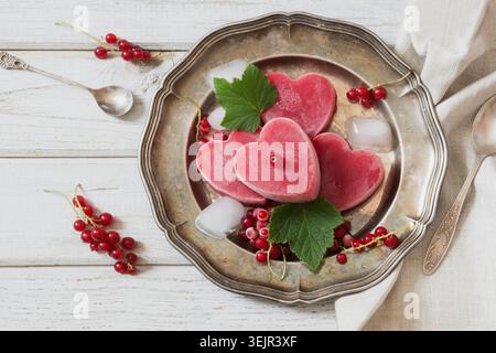 Glace maison de groseille rouge en forme de coeur et sur plat vintage et fond en bois. Vue de dessus. Boissons glacées. Banque D'Images