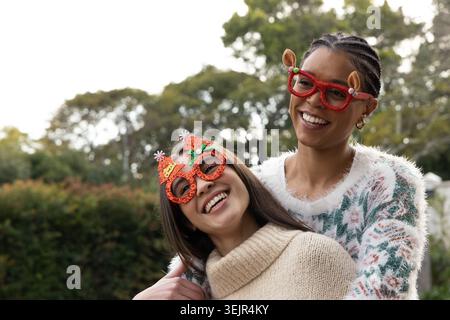 Amies afro-américaines et asiatiques posant dans le parc portant des lunettes de vacances rouges et des tricots. Lunettes, chandails, extérieur, Candid, bokeh, mode Banque D'Images