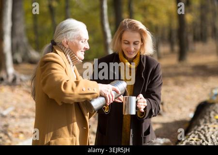 Deux amies femmes boivent du thé et profitent de vacances en automne en plein air. portrait d'une femme âgée souriante avec une fille adulte Banque D'Images