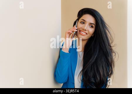 Heureuse jeune étudiante parle par téléphone portable après examen, partage son succès. Brune femme entrepreneure aime les convers téléphoniques Banque D'Images