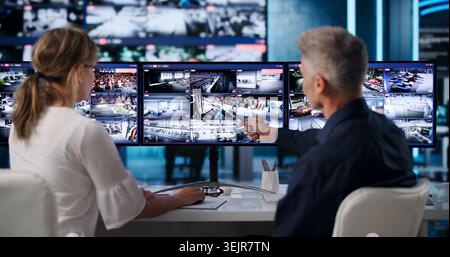 Deux gardes de sécurité surveillent plusieurs écrans de vidéosurveillance dans la salle de contrôle occupée. Banque D'Images