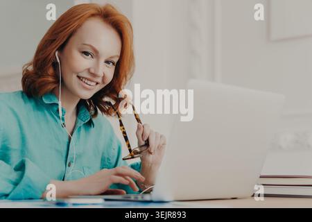 Jeune femme utilisant un ordinateur portable avec des écouteurs souriant pendant la réunion en ligne à la maison Banque D'Images